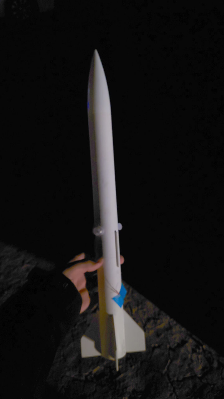 A photo of George-L taken at night showing the two lights attached to the sides of the rocket and the igniter leads taped to the side of the rocket.